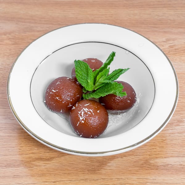 Five Gulab Jamun, Indian fried dough balls, garnished with mint and coconut flakes in a white bowl.
