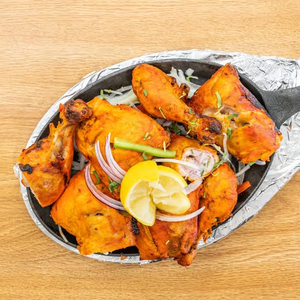 Vatica Indian Cuisine's Tandoori Chicken, garnished with lemon, onions, and green chilies, served in a hot skillet.