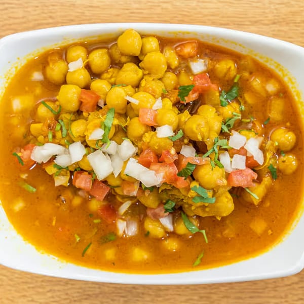 A close-up of Vatica Indian Cuisine's chana masala, garnished with diced tomatoes, onions, and cilantro.