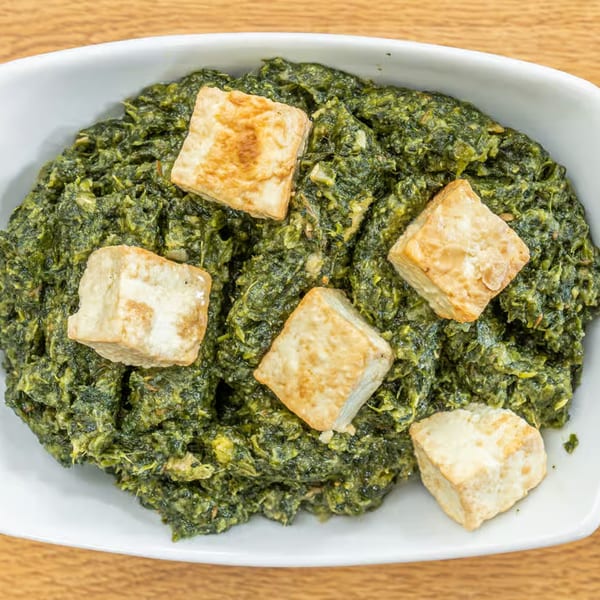 A white bowl filled with vibrant green Palak Paneer, topped with five golden-brown paneer cubes.