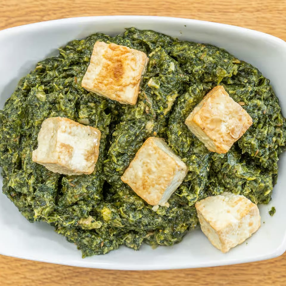 A white bowl filled with vibrant green Palak Paneer, topped with five golden-brown paneer cubes.